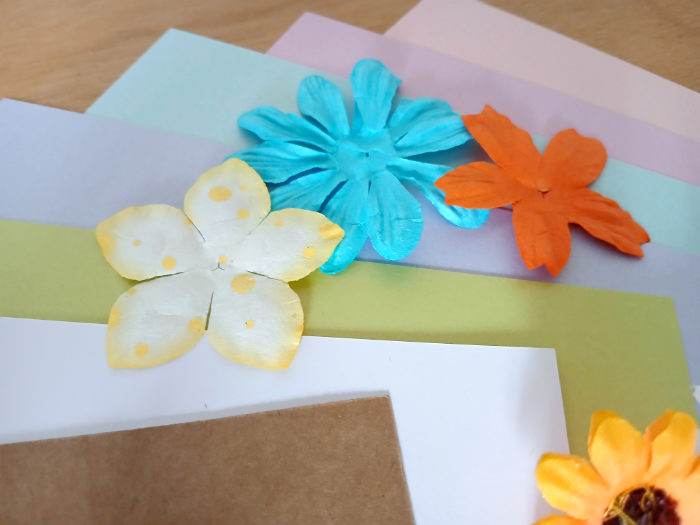 A photo of some different coloured paper stock and paper flowers for cardmaking.