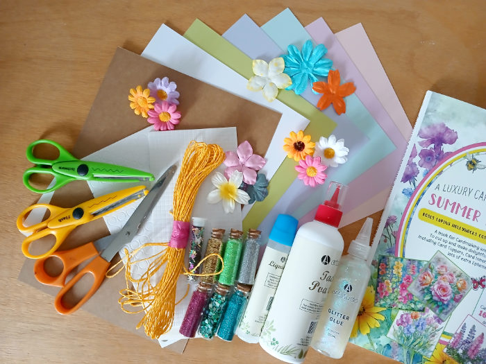 A collection of arts and crafts materials including scissors, paper flowers, glitter, string, glue and sticky foam craft pads.
