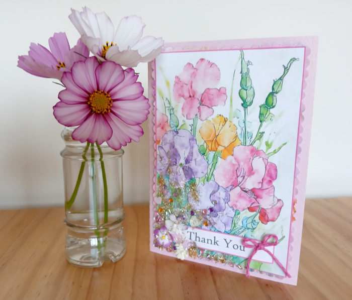 A photo of the finished hand-crafted card next to a small vase of cosmos flowers. An example of a card that can be made from "Summer Flowers - A Luxury Card Making Book" by Kay Burton.