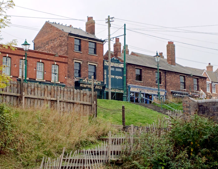 A full-colour photograph of a street view in the Black Country Living Museum in Dudley. The image shows a row of commercial buildings on a hill, with steps leading to the foreground.