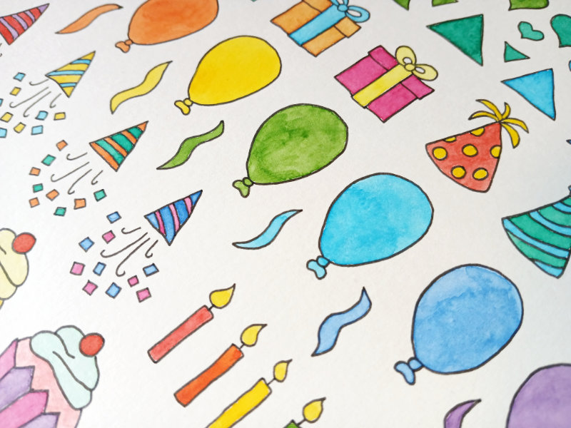 A close up of some of the colourful watercolour designs by Ruth Burton. There are illustrations of balloons, presents, party hats, candles, cupcakes and party poppers.