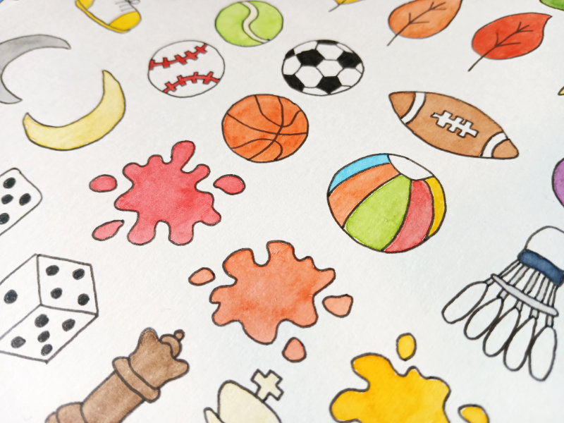 A close up of some of the colourful watercolour designs by Ruth Burton. There are illustrations of sports equipment, games pieces, leaves, paint splotches and moons.