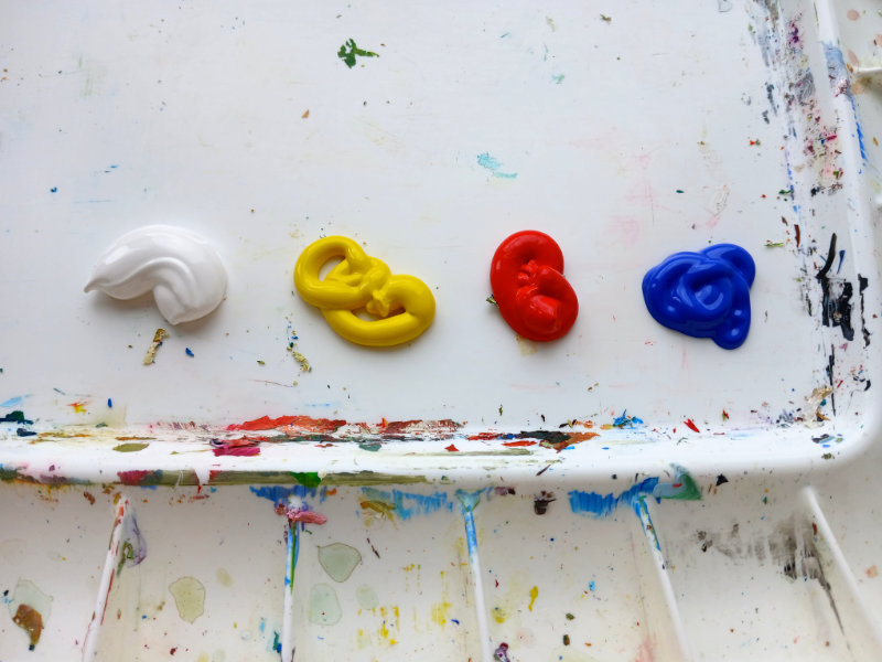 A paint palette of fours acrylic paints: titanium white, lemon yellow, brilliant red, ultramarine blue.