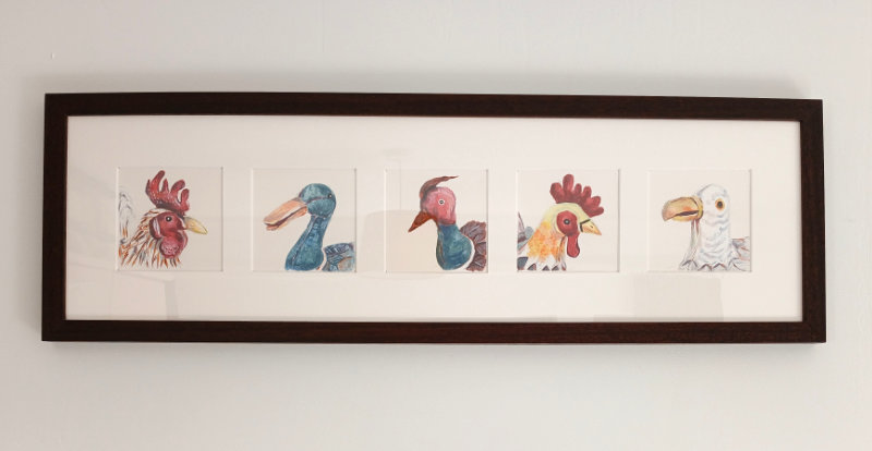 The bird paintings in a dark wood frame hanging on the wall. From left to right the birds are cockerel, duck, pheasant, chicken, seagull.